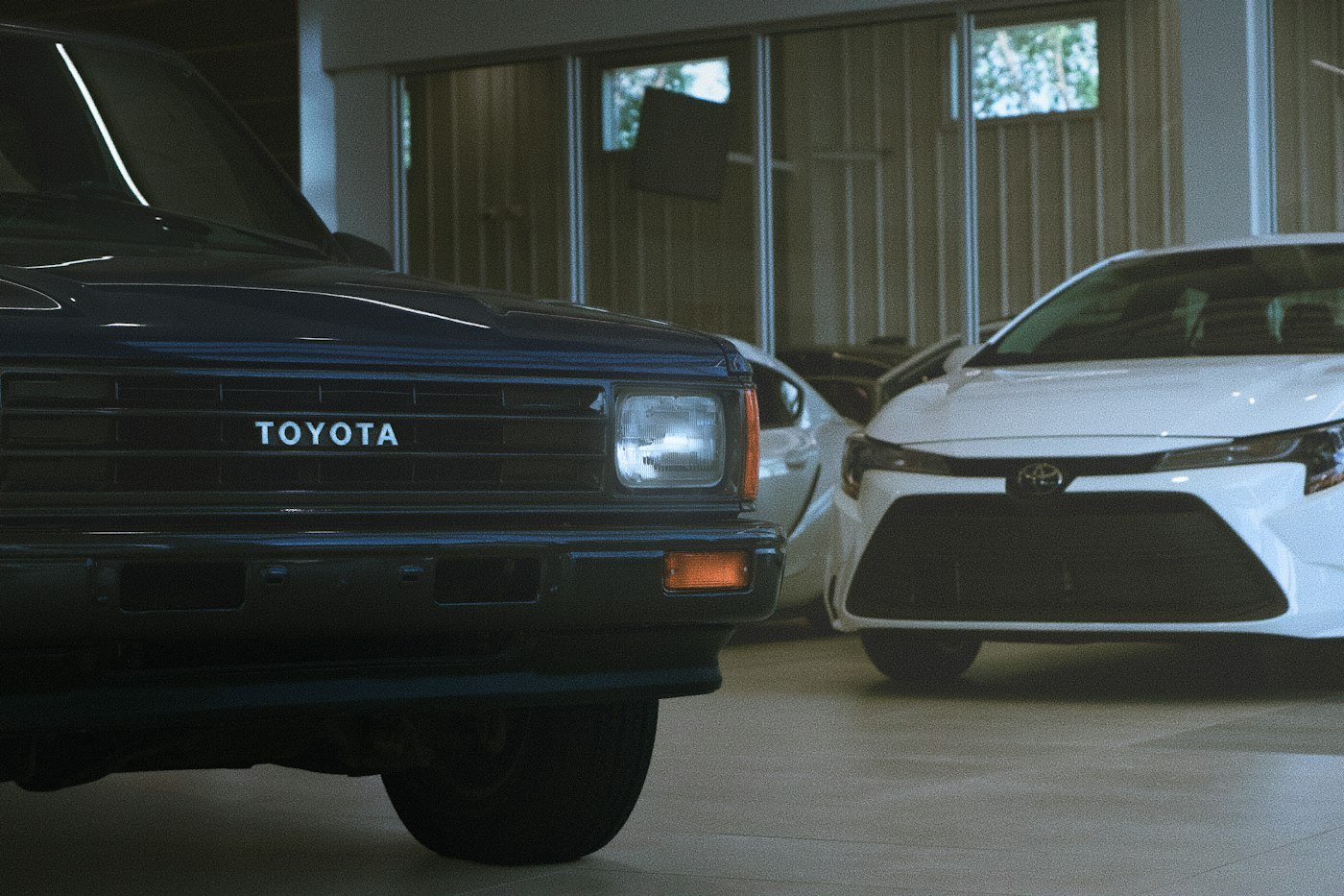 An older Toyota pickup and a white Toyota saloon parked in a car showroom