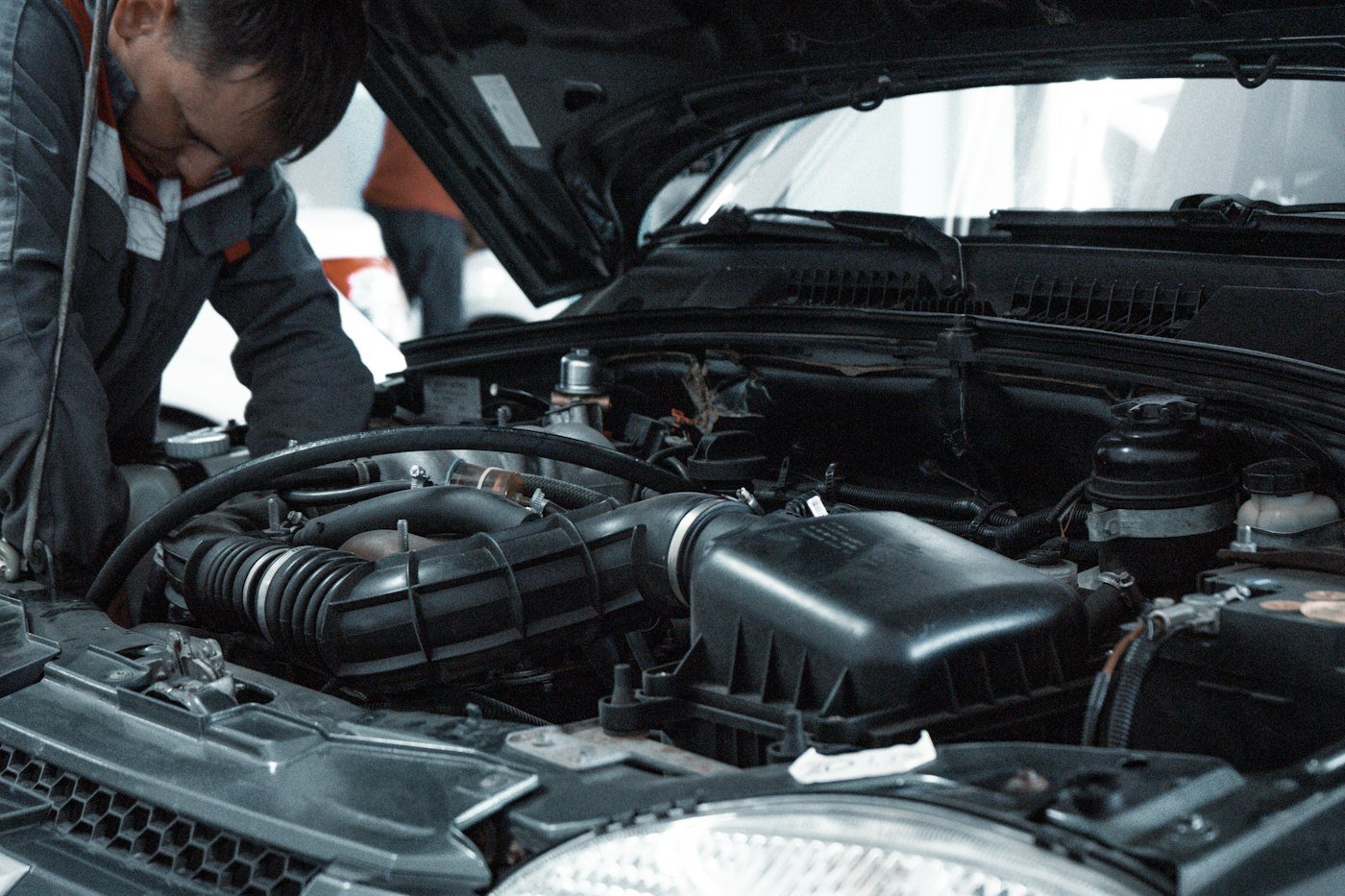 Mechanic in a grey uniform inspecting a car engine in a workshop
