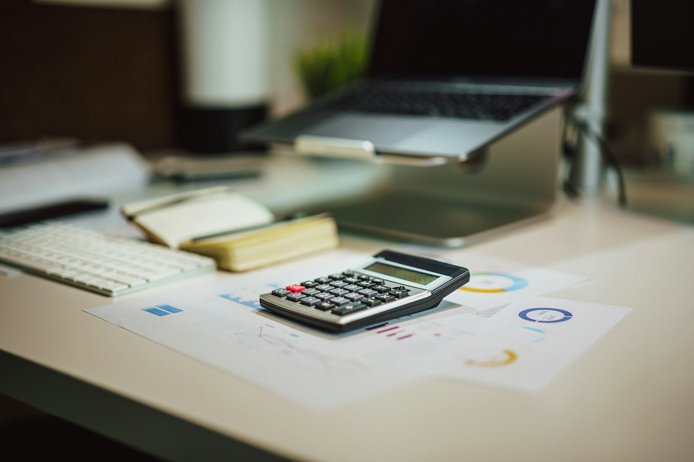 Calculator on printed financial charts in front of a laptop on a desk